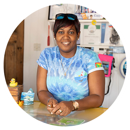 A woman in a blue shirt is smiling at a table after scuba diving in Grenada.