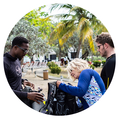 A group of people looking at scuba gear in a park, excited for their next adventure with eco dive Grenada. A group of people looking at scuba gear in a park, excited for their next adventure with eco dive Grenada.